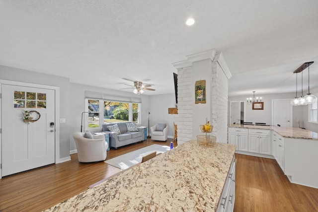 kitchen featuring white cabinetry, hanging light fixtures, light stone counters, ceiling fan with notable chandelier, and light wood-type flooring