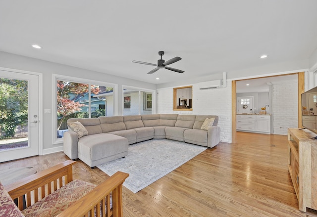 living room featuring ceiling fan, light hardwood / wood-style flooring, brick wall, and a wall mounted air conditioner