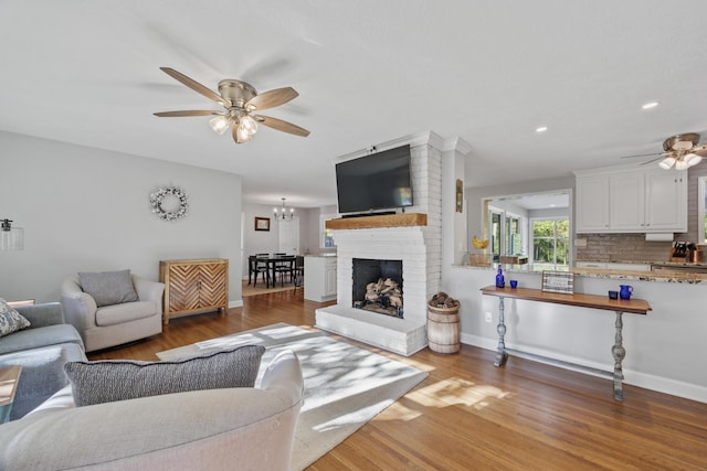 living room with a fireplace, ceiling fan with notable chandelier, and hardwood / wood-style flooring