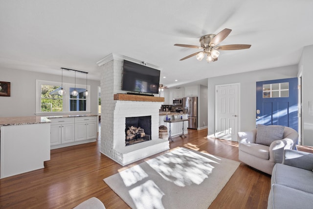 living room featuring ceiling fan, dark wood-type flooring, and a brick fireplace