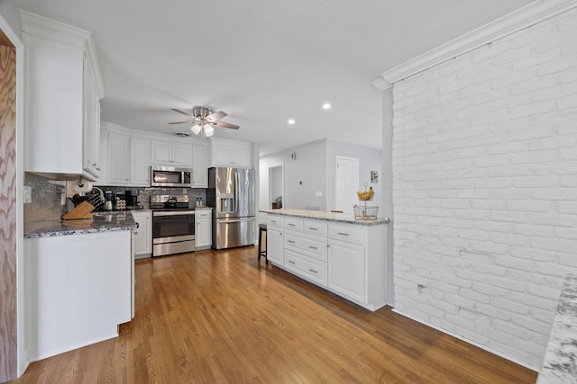 kitchen featuring white cabinets, appliances with stainless steel finishes, decorative backsplash, and light stone counters