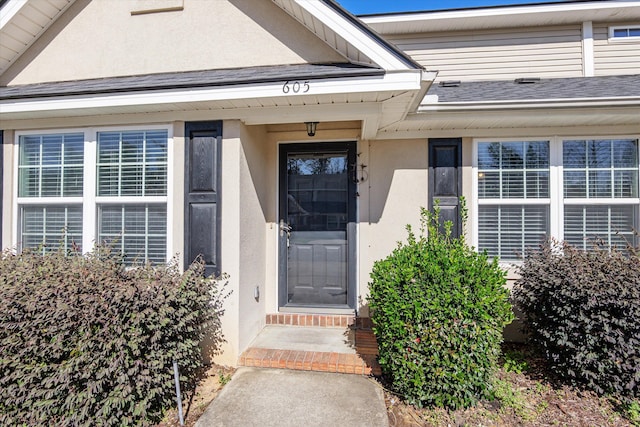 property entrance featuring a shingled roof and stucco siding