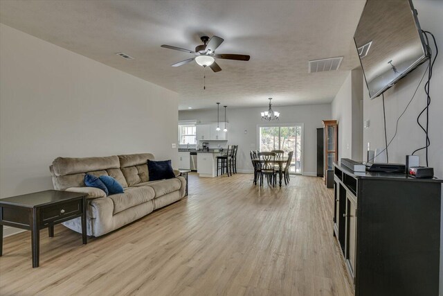 living room featuring ceiling fan with notable chandelier, light wood-type flooring, and a textured ceiling