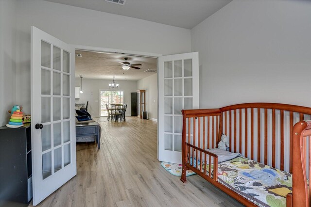 bedroom featuring french doors, light hardwood / wood-style floors, and ceiling fan with notable chandelier