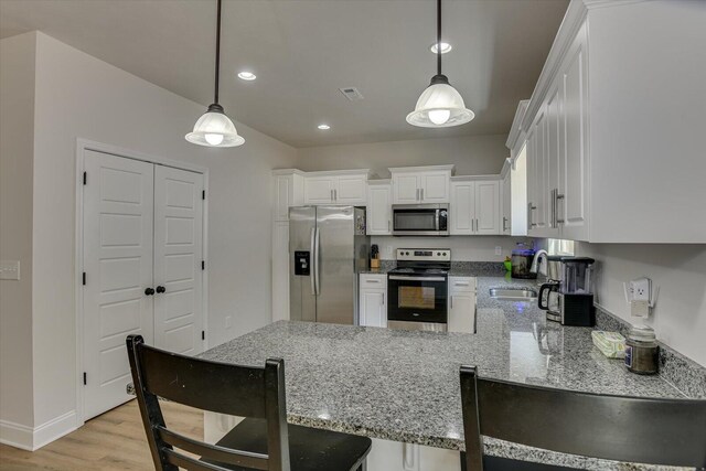 kitchen with kitchen peninsula, stainless steel appliances, sink, decorative light fixtures, and white cabinetry