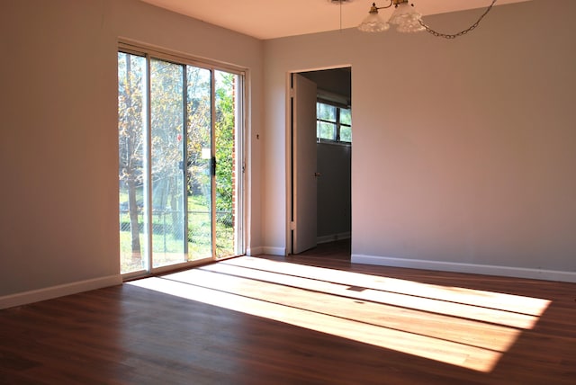 spare room featuring dark wood-type flooring and an inviting chandelier