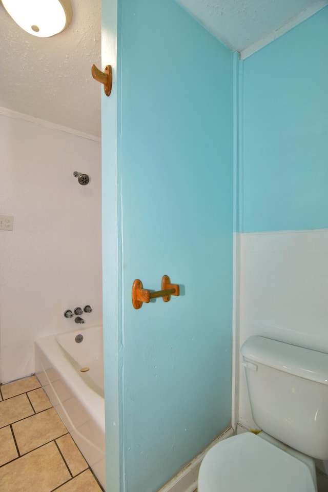 bathroom with tile patterned floors, a tub to relax in, a textured ceiling, and toilet