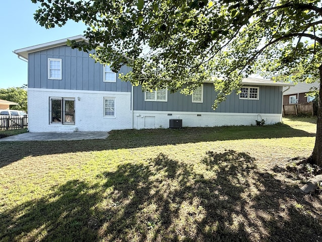 rear view of house with a lawn, board and batten siding, fence, cooling unit, and a patio area