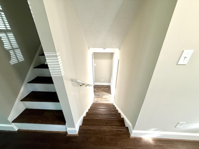 stairs featuring a textured ceiling, baseboards, and wood finished floors