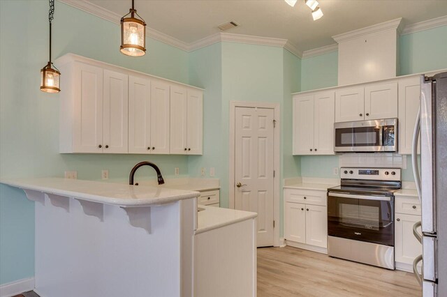 kitchen featuring kitchen peninsula, white cabinetry, stainless steel appliances, and decorative light fixtures