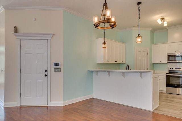 kitchen with kitchen peninsula, ornamental molding, stainless steel appliances, white cabinetry, and a breakfast bar area