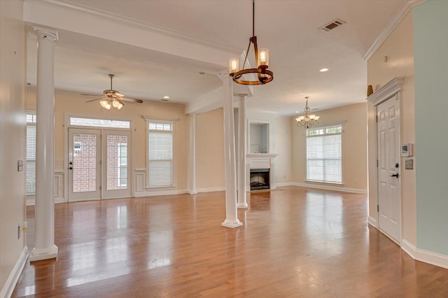 unfurnished living room featuring ceiling fan with notable chandelier, light wood-type flooring, decorative columns, and crown molding