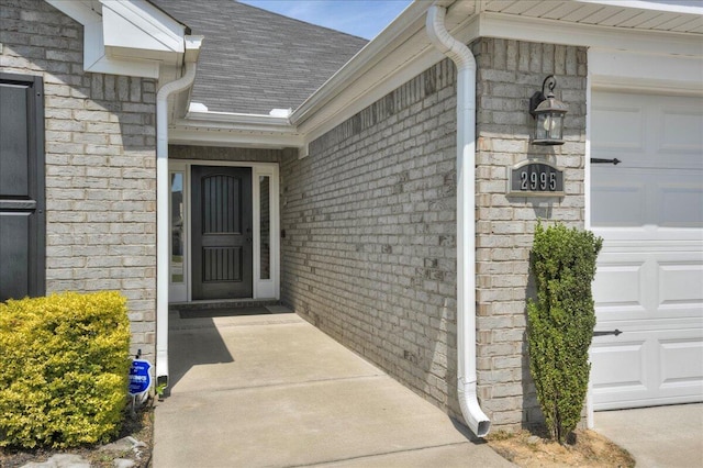 entrance to property with stone siding, roof with shingles, and a garage