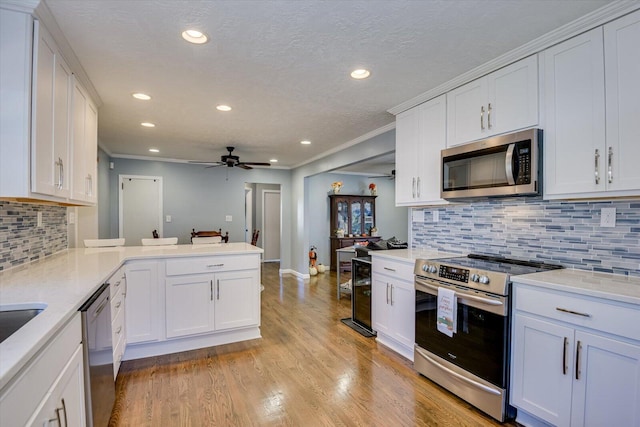 kitchen with kitchen peninsula, light hardwood / wood-style flooring, ceiling fan, appliances with stainless steel finishes, and white cabinetry