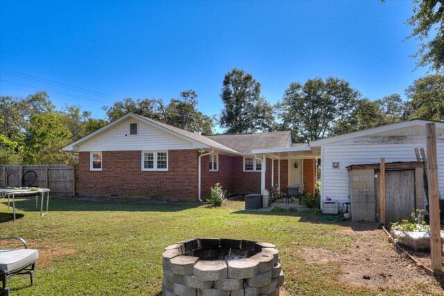 back of house with a yard, a trampoline, a fire pit, and cooling unit