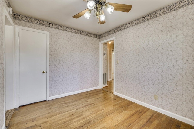 empty room featuring wallpapered walls, a ceiling fan, baseboards, and wood finished floors