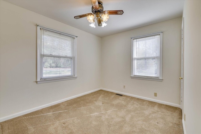 carpeted empty room featuring a ceiling fan, a wealth of natural light, visible vents, and baseboards