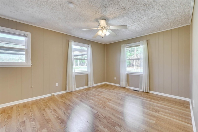 empty room with a wealth of natural light, a textured ceiling, baseboards, and wood finished floors