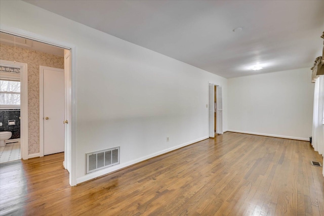 empty room featuring baseboards, visible vents, and hardwood / wood-style floors