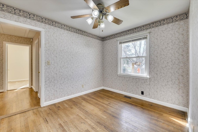 empty room with visible vents, baseboards, hardwood / wood-style floors, attic access, and wallpapered walls