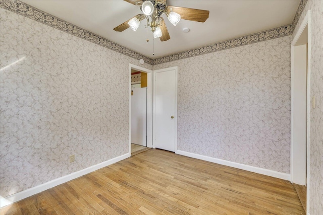 spare room with baseboards, wood finished floors, a ceiling fan, and wallpapered walls