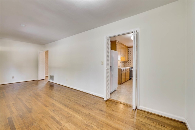 spare room with light wood-type flooring, visible vents, and baseboards