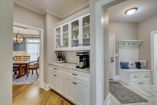 bar featuring light wood-type flooring, decorative backsplash, crown molding, and an inviting chandelier