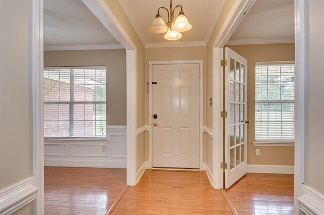 foyer with light hardwood / wood-style floors, crown molding, and an inviting chandelier