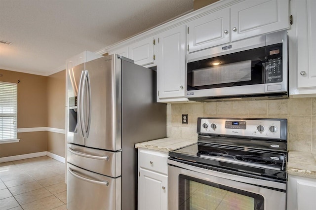 kitchen with white cabinets, light stone countertops, light tile patterned floors, ornamental molding, and stainless steel appliances