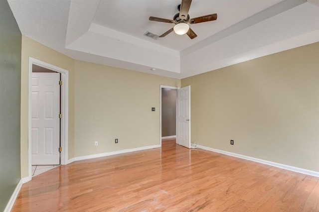 unfurnished room featuring ceiling fan, light hardwood / wood-style flooring, and a tray ceiling