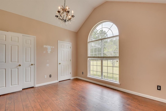 empty room with a chandelier, wood-type flooring, and lofted ceiling