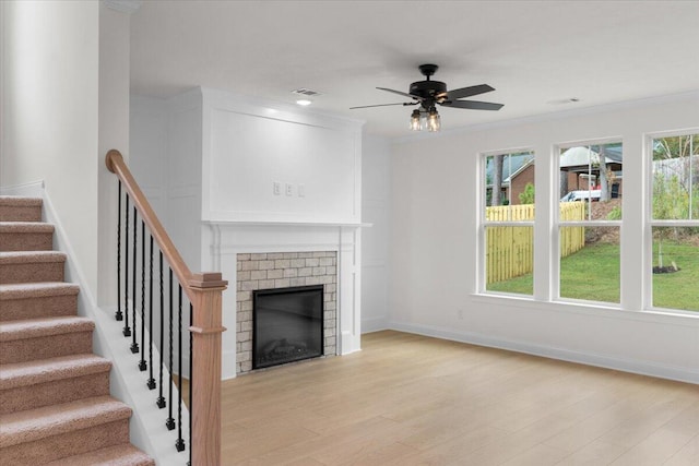 unfurnished living room with ceiling fan, light wood-type flooring, crown molding, and a brick fireplace