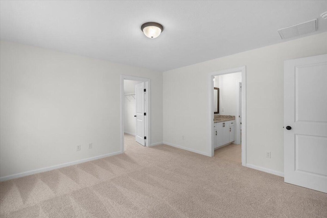 unfurnished bedroom with a closet, a spacious closet, light carpet, and ensuite bath