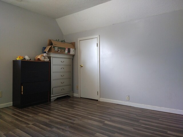 unfurnished bedroom featuring lofted ceiling, a textured ceiling, and dark wood-type flooring