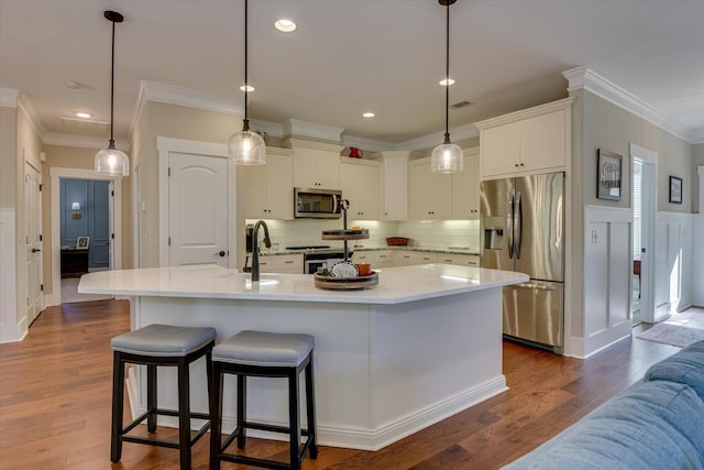 kitchen with dark wood-type flooring, pendant lighting, a center island with sink, white cabinets, and appliances with stainless steel finishes