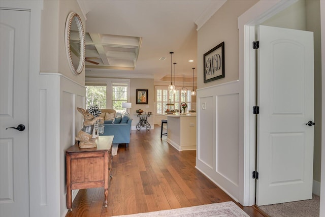 corridor with coffered ceiling, crown molding, hardwood / wood-style flooring, beamed ceiling, and a chandelier