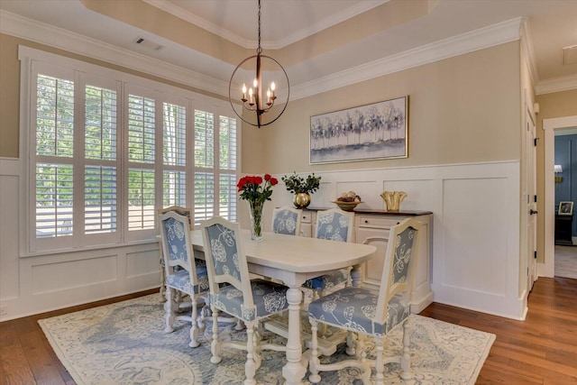 dining room with hardwood / wood-style flooring, a healthy amount of sunlight, a raised ceiling, and an inviting chandelier