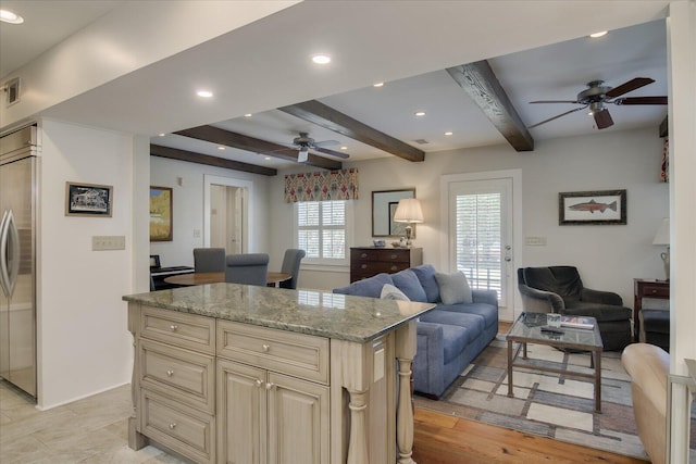 kitchen featuring a center island, cream cabinets, light stone countertops, beamed ceiling, and stainless steel built in refrigerator