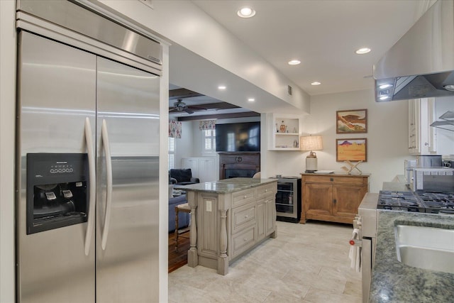 kitchen featuring light stone countertops, a center island, a kitchen breakfast bar, built in fridge, and ventilation hood