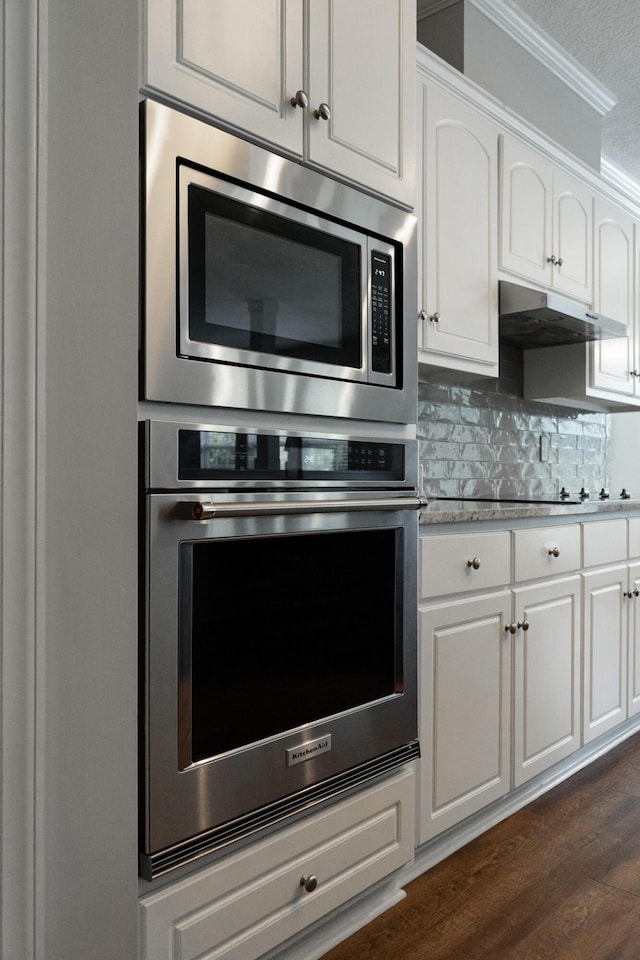 724 Avrett Cir, Evans, GA 30809 - kitchen with appliances with stainless steel finishes, under cabinet range hood, ornamental molding, white cabinetry, and tasteful backsplash