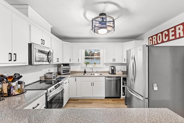 kitchen featuring appliances with stainless steel finishes, sink, white cabinets, light stone counters, and a textured ceiling