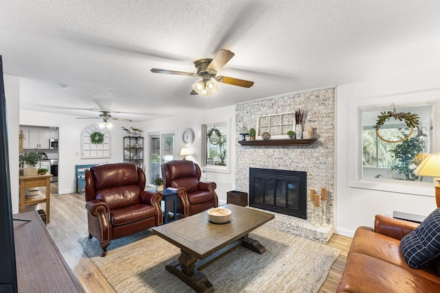 living room with ceiling fan, a brick fireplace, a textured ceiling, and light wood-type flooring