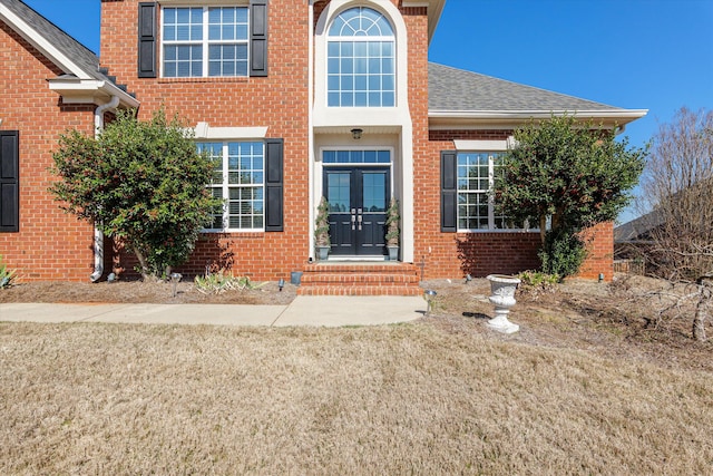 doorway to property with roof with shingles, french doors, a lawn, and brick siding