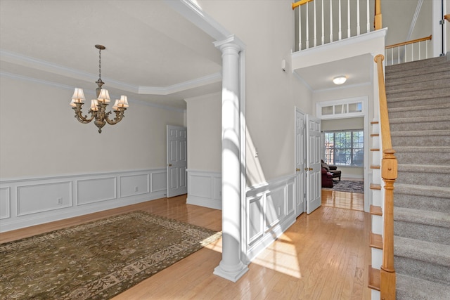 foyer with wood finished floors, stairs, ornamental molding, ornate columns, and an inviting chandelier