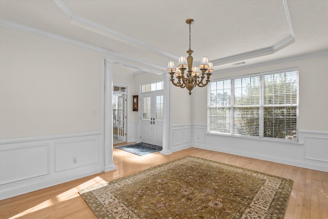 unfurnished dining area featuring light wood-style floors, ornamental molding, a raised ceiling, and wainscoting