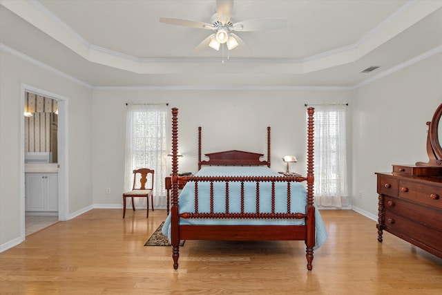 bedroom with light wood-style flooring, visible vents, a tray ceiling, and baseboards