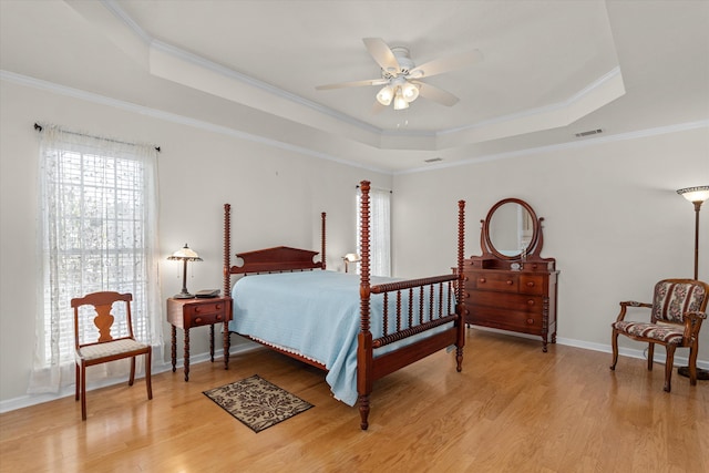 bedroom featuring light wood finished floors, a raised ceiling, visible vents, and crown molding