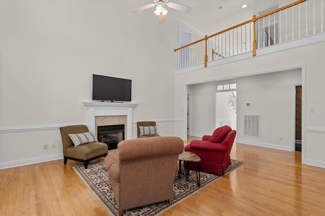 living area with a glass covered fireplace, wood-type flooring, visible vents, and ceiling fan