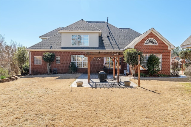 back of property with a yard, brick siding, a patio, and a shingled roof