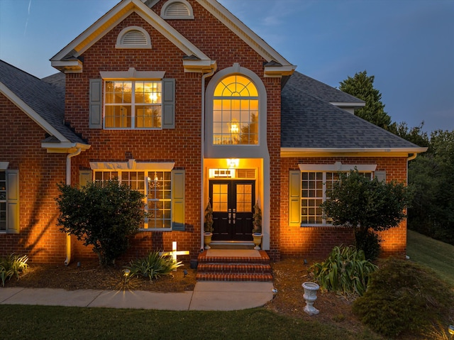 traditional-style house featuring french doors, brick siding, and roof with shingles